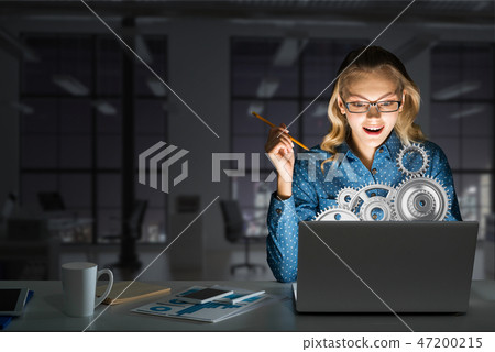 Attractive blonde wearing glasses in dark office using laptop. Mixed media Attractive blonde wearing glasses in dark office using laptop. Mixed media 47200215