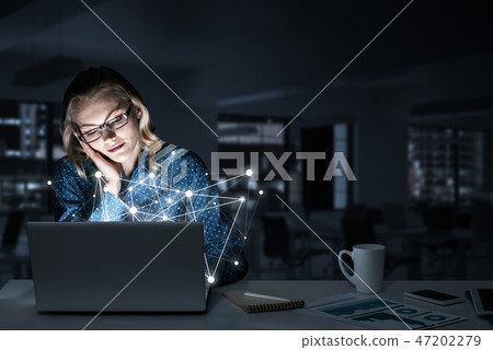 Attractive blonde wearing glasses in dark office using laptop. M Attractive blonde wearing glasses in dark office using laptop. M 47202279