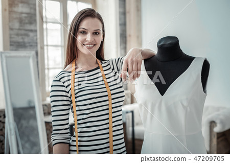 Beaming fashion designer smiling while standing near dress form 47209705