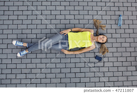 Young woman in a T-shirt with listening music and lies on the pavement 47211807