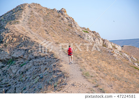 rear view of athletic runner running on a mountain trail on a blue sky background rear view of athletic runner running on a mountain trail on a blue sky background 47224581