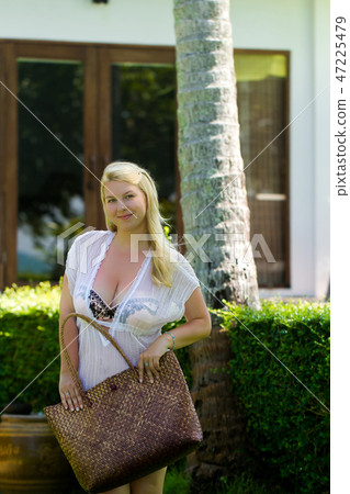 Young blonde beautiful woman in see-through beach dress and bikini near luxury tropical villa with 47225479