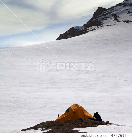 Hiker sitting near camping tent in snowy mountains Hiker sitting near camping tent in snowy mountains 47226913