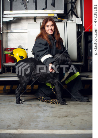 Image of female firefighter with black dog sitting on background of fire truck 47239181