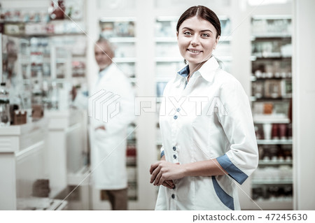 Appealing green-eyed pharmacist smiling while meeting clients in drugstore Appealing green-eyed pharmacist smiling while meeting clients in drugstore 47245630