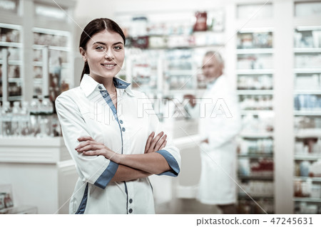 Dark-haired beaming appealing woman wearing white coat working in drugstore Dark-haired beaming appealing woman wearing white coat working in drugstore 47245631