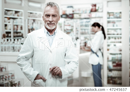 Senior pharmacist coming to the drugstore checking the work of his employees Senior pharmacist coming to the drugstore checking the work of his employees 47245637