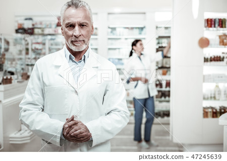 Bearded mature man with facial wrinkles feeling busy standing in his drugstore 47245639