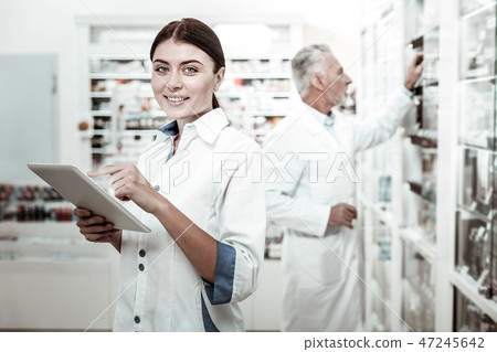 Beaming blue-eyed female pharmacist wearing white coat feeling cheerful Beaming blue-eyed female pharmacist wearing white coat feeling cheerful 47245642