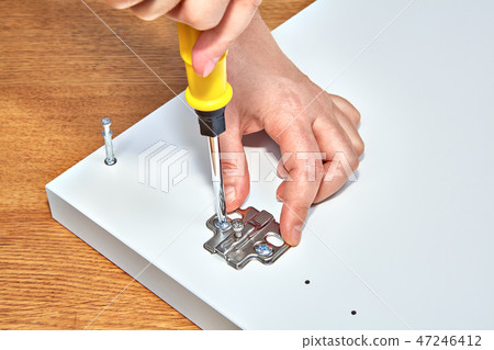 Handyman fixes furniture door hinges of table. 47246412