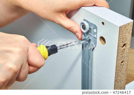 Furniture assembler tightens screw in drawer slide 47246417