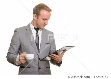 Handsome Caucasian businessman reading clipboard while drinking  47249147