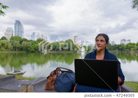 Portrait of mature Indian woman at park using laptop computer Portrait of mature Indian woman at park using laptop computer 47249305