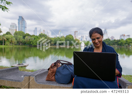 Portrait of mature Indian woman at park using laptop computer Portrait of mature Indian woman at park using laptop computer 47249313