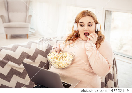 Unpleasant plus-size woman watching movie on her laptop Unpleasant plus-size woman watching movie on her laptop 47252149
