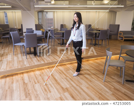 Visually impaired business woman walking in the office using white cane 47253005