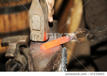 Blacksmith working metal with hammer on the anvil 47259983
