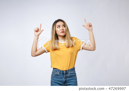 Young Asian woman looking angry and sad while pointing finger at camera isolated against white Young Asian woman looking angry and sad while pointing finger at camera isolated against white 47269997