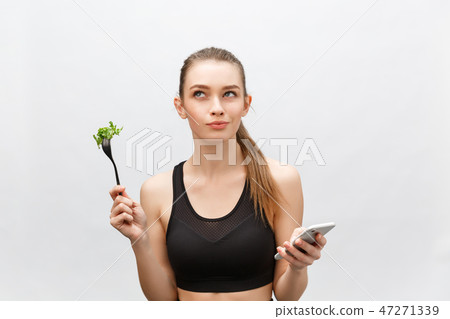 Beautiful young woman wearing sport clothes with salad in hand, using smart phone. Beautiful young woman wearing sport clothes with salad in hand, using smart phone. 47271339