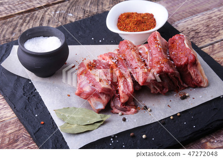 Raw fresh meat, uncooked lamb or beef ribs with pepper, garlic, salt and spices on dark stone Raw fresh meat, uncooked lamb or beef ribs with pepper, garlic, salt and spices on dark stone 47272048