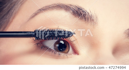 Young woman applying mascara to her lashes. 47274994