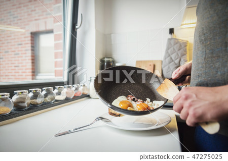 Man putting fried eggs on the plate 47275025