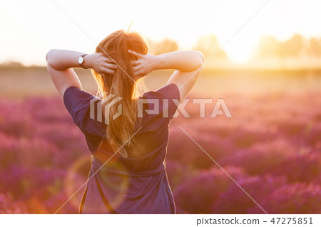 Young woman touching her long sombre hair looking at lavender field at sunset Young woman touching her long sombre hair looking at lavender field at sunset 47275851