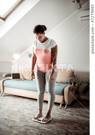 Attentive curly woman standing on white weights 47279093