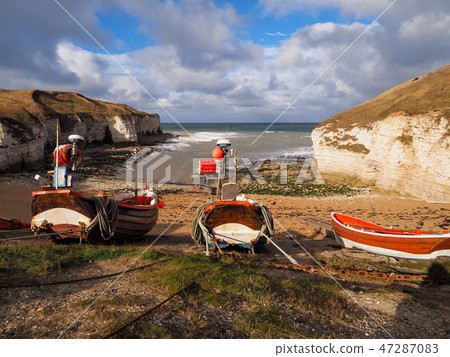 Colorful red and white fishing boats tied up on the beach waiting for the tide with white cliffs Colorful red and white fishing boats tied up on the beach waiting for the tide with white cliffs 47287083