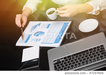 Businesswoman with coffee and pen points to graph 47287608