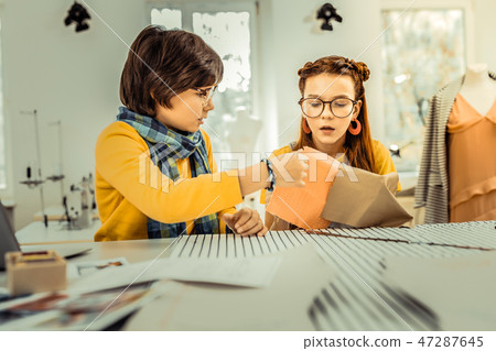 Boy wearing blue scarf giving his sister some pieces of fabric 47287645