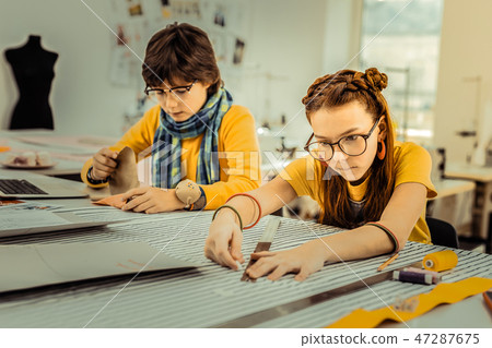 Red-haired girl wearing glasses and massive earrings using ruler 47287675