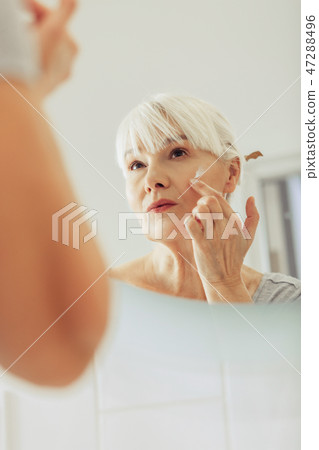 Pleasant nice woman applying cream on her face 47288496