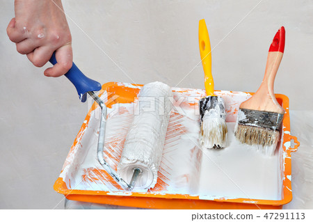 Hands painter dunks roller brush in tray of paint. 47291113