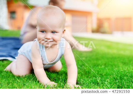 Portrait of cute little caucasian boy having fun in garden with mother. Child crawling on green Portrait of cute little caucasian boy having fun in garden with mother. Child crawling on green 47291550