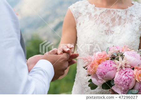 the groom puts the ring on the bride's finger 47296027