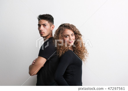 Portrait of a young couple standing back to back in a studio, wearing black clothes. Portrait of a young couple standing back to back in a studio, wearing black clothes. 47297561