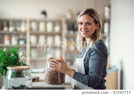 A female shop assistant in a zero waste shop, holding a jar with groceries.