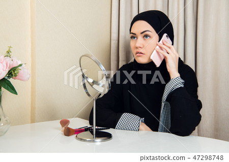 cheerful happy pretty muslim woman sitting and using mobile cell phone calling for friend chatting 47298748