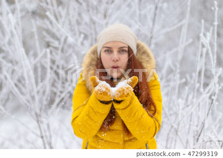 Happy girl in winter clothes blowing on palms 47299319