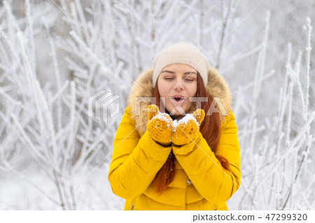 Happy girl in winter clothes blowing on palms 47299320