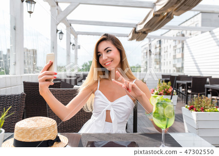Beautiful girl sitting in a cafe on veranda. In the summer in the city on a sunny day. Photographs 47302550