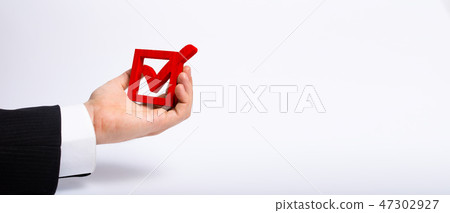 The hand holds a wooden check box with a tick 47302927