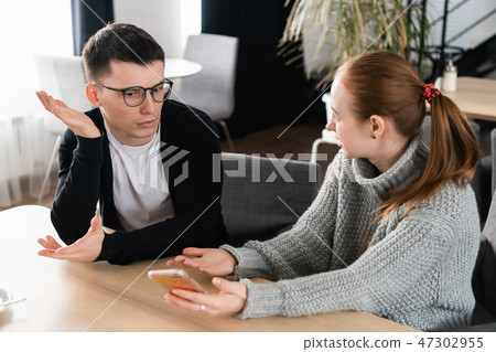 Girlfriend asking for explanation of her boyfriend sitting on a couch in the cafe Girlfriend asking for explanation of her boyfriend sitting on a couch in the cafe 47302955