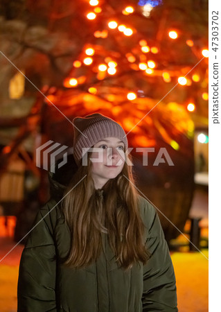 Beautiful girl looking down on the night city street against the backdrop of glowing storefront Beautiful girl looking down on the night city street against the backdrop of glowing storefront 47303702