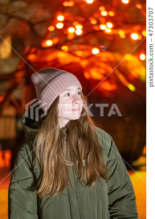 Beautiful girl looking down on the night city street against the backdrop of glowing storefront 47303707