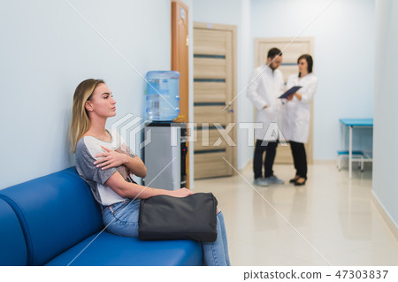 Woman waiting at a hospital hallway for a test results. Feeling nervous. Doctors talking on a 47303837