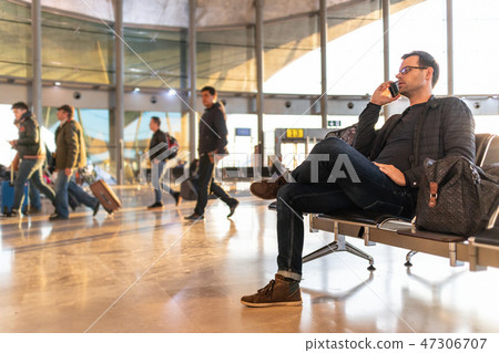 Male traveler talking on his cell phone while waiting to board a plane at departure gates at airport 47306707