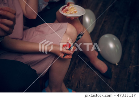 Close up of girl's hand holding a fork with a piece of cake on her knees 47313117