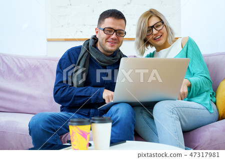 Man and woman sit on the couch, chatting and using a desktop computer. 47317981